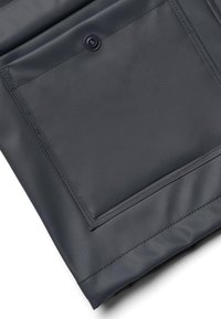 Gros plan sur la manche d'une veste en cuir noire montrant une poche carrée avec une fermeture à bouton-pression et des coutures détaillées.