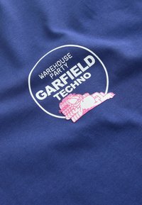 Tissu bleu avec un logo circulaire blanc portant l'inscription « Warehouse Party Garfield Techno » et un Garfield rose de dessin animé allongé et détendu sous le texte.