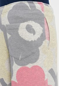 Šedé jogger nohavice s kvetinovým vzorom majú vrecko a jemnú textúru, s veľkými kvetinovými motívmi v odtieňoch šedej, ružovej a béžovej.