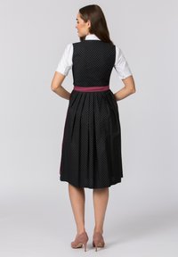 Schwarzes, gemustertes Kleid mit einem taillierten Oberteil und einem plissierten Rock, akzentuiert durch einen rosa Riegelgürtel; hat kurze Ärmel und einen Knopfkragen.