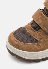Bruine suede en mesh schoen met twee klittenbandsluitingen, voorzien van een gestructureerde buitenzool en verstevigde neus. Ontworpen voor comfort en duurzaamheid.