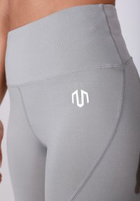 Leggings haute taille gris avec une texture lisse, présentant un logo blanc sur la cuisse gauche et des coutures plates pour le confort.