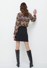 Halenka s dlouhými rukávy se vzorem cik-cak v hnědé, modré a béžové barvě, kombinovaná s černou mini sukní a lesklými černými kozačkami pod kolena.
