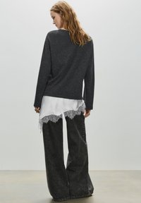 Grå langærmet top med en hvid lagdelt undertrøje med blonderkant, kombineret med vidde bukser i mørk denim. Glat stoftekstur.