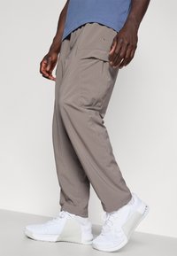 Pantaloni cargo gri, cu o croială relaxată și buzunare laterale. Purtați cu încălțăminte sport albă. Materialul are o aparență moale, texturată.