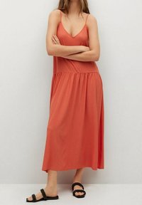 Robe maxi couleur rouille avec un corsage ajusté, des bretelles spaghetti réglables et une taille froncée. Portée avec des sandales plates noires.
