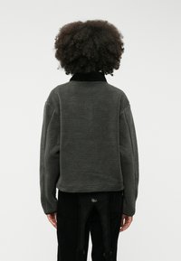 Γκρι fleece πουλόβερ με ψηλό γιακά και υφή στην επιφάνεια. Διαθέτει άνετη εφαρμογή και χαμηλούς ώμους. Απλό σχέδιο, χωρίς ορατά μοτίβα.