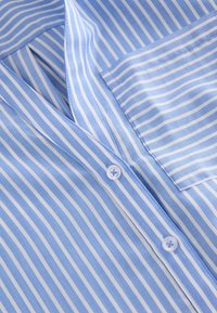 Chemise boutonnée à rayures verticales bleues et blanches avec une poche poitrine et des boutons blancs le long de la patte de boutonnage.