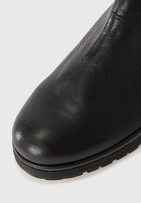Bottette en cuir noir avec un bout arrondi, une texture lisse et une semelle en caoutchouc épaisse. Aucune décoration ni motif visible.