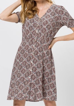 Femme portant une robe boutonnée au genou, à manches courtes, avec un motif floral géométrique rouge et blanc.