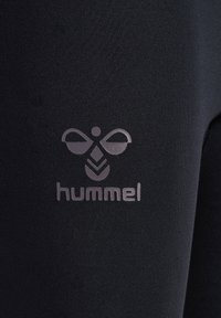 Svarta atletiska leggings med en reflektiv Hummel-logotyp på den nedre delen, tillverkade av mjukt, stretchigt tyg med matt yta.
