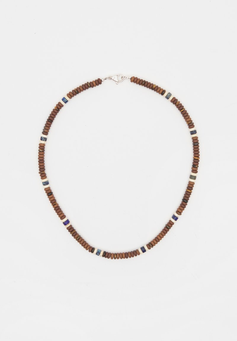 Brun pärlhalsband bestående av cirkulära träpärlor, blandat med vita och mörkblå accentpärlor, med en silverklämma.