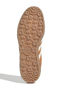 Adidas sneakersålsystem med en glat beige gummibase, cirkulære mønstre og et centralt logo. Tre hvide striber på siden.