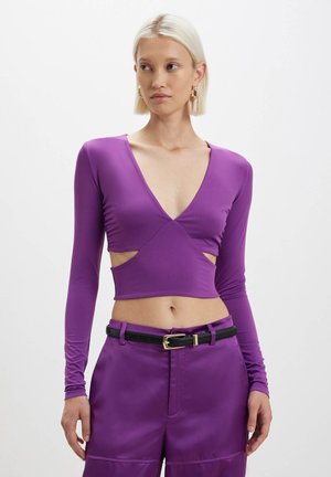 Top corto a maniche lunghe viola con scollatura a V profonda e tagli laterali. Realizzato in tessuto morbido, presenta un design aderente e una texture leggera.