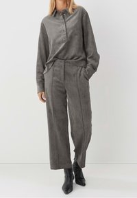 Camicia in corduroy grigio con colletto a bottoni e maniche lunghe, abbinata a pantaloni larghi in corduroy grigio, entrambi caratterizzati da una texture morbida.