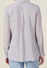 Tylny widok koszuli z długim rękawem, przedstawiającej geometryczny wzór w odcieniach niebieskiego i czerwonego, z kołnierzykiem i guzikami przy mankietach.