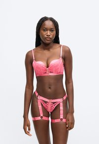 Roze satijnen lingerieset met een gevoerde beha met kanten details en verstelbare bandjes, vergezeld van een bijpassende jarretelriem met gouden accenten.