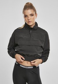 Juodas trumpas švarkas, pagamintas iš lengvos medžiagos, su pusiau užtrauktuku, elastingomis rankovėmis ir priekinėmis kišenėmis. Derinamas su juodomis leggingomis.