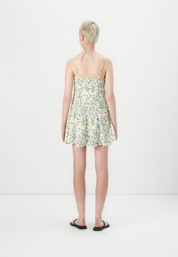 Blommig solklänning med figursydd bodice, utsvängd kjol, justerbara band och en knytning bak. Färgerna inkluderar gult, grönt och vitt.