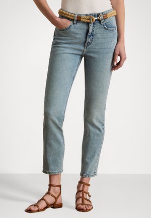 Hellblaue Jeans mit geradem Schnitt und hoher Taille, kombiniert mit einem hellen geflochtenen Gürtel. Mit fünf Taschen und einem dezenten Waschungseffekt. Braune Riemchen-Sandalen.
