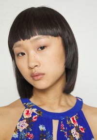 Top halter azul com padrão floral em vermelho, rosa e azul. O tecido é leve e apresenta um acabamento texturizado. Apresenta um detalhe em forma de buraco na gola.