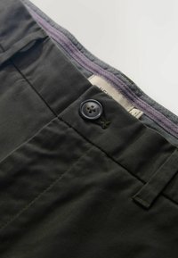 Sötétzöld pamut anyagú nadrág gombos záródással, övhurkokkal és finom textúrával. A derékpánt belső része eltérő színű.