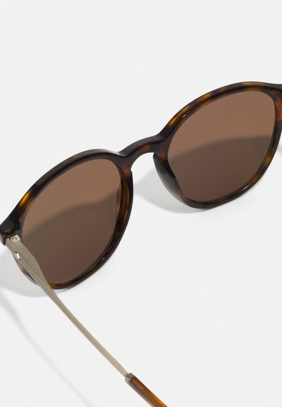 Round sunglasses with brown lenses and tortoiseshell frames. Thin metal temples connected to the frame, with a smooth finish.