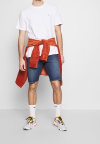 Valkoinen puuvillainen T-paita, oranssit corduroy-housut solmittuna vyötärölle, farkkushortsit sekä valkoiset lenkkarit, joissa on keltaisia ja mustia yksityiskohtia.