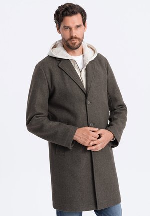 Dark green wool coat with a notched collar, two buttons, side pockets, and a textured finish, layered over a light hoodie.