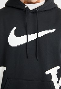 Μαύρη φούτερ φτιαγμένη από μείγμα βαμβακιού, με μεγάλο λευκό εικονογράφημα λογότυπο Nike και λευκή κείμενη λεπτομέρεια στο μπροστινό μέρος. Με κουκούλα με κορδόνι.