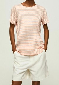 Lyserød og hvidstribet t-shirt lavet af letvægtsbomuld, med rund halsudskæring og korte ærmer, parret med hvide skræddersyede shorts.