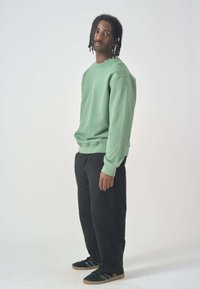 Green cotton sweatshirt with a ribbed crew neck and cuffs, paired with black wide-leg pants and black sneakers with gum soles.