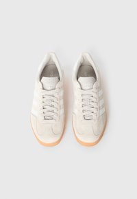 Biele semišové tenisky s tromi bielymi pruhmi, zaobleným tvarom, textúrovanými detailmi a podrážkou z gumy. Vo vnútri sa nachádza detail s logom.