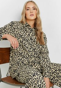 Beige en zwarte leopardprint shirt en broek set van stof. Het shirt heeft een kraag en lange mouwen, met een losse pasvorm.