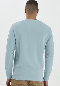 Lichtblauwe sweatshirt met lange mouwen, geribbelde manchetten en zoom, met een vierkante schouderontwerp en een gladde textuur. Achteraanzicht weergegeven.