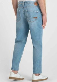 Jeans in denim azzurro chiaro con una vestibilità comoda, dotati di tasche posteriori e di una patch in pelle beige sulla vita. Sneakers bianche completano il look.