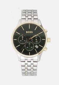 Reloj cronógrafo con un dial negro, acentos dorados, pulsera de metal plateado, tres sub-diales y una pantalla de fecha a las 6 en punto.