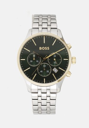 Montre chronographe avec un cadran noir, des accents dorés, un bracelet en métal argenté, trois sous-cadrans et un affichage de la date à 6 heures.