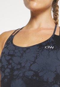 Μαύρο και ναυτικό αθλητικό τοπ με σχέδιο tie-dye, λεπτές τιράντες στους ώμους και λογότυπο “ICIW” στην αριστερή πλευρά. Υφασμάτινη ύφανση.