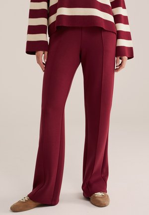 Person trägt burgunderrote weite Hosen, beige und braune Sneakers und ein burgunderrotes und cremefarben gestreiftes Langarmshirt.