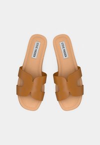 Paire de sandales à enfiler en cuir caramel avec des brides découpées et étiquette Steve Madden, présentées sur un fond blanc.