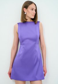 Violet mekko ilman hihoja, jossa on tiukka yläosa ja levenevä helma. Tasainen pinta, polven pituinen, jossa on minimaalinen sauma ja korkea kaula-aukko.