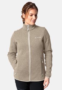 Giacca in pile beige con colletto alto, zip frontale completa, due tasche laterali e cuciture bianche a contrasto lungo le cuciture.