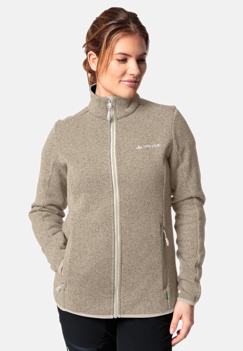 Giacca in pile beige con colletto alto, zip frontale completa, due tasche laterali e cuciture bianche a contrasto lungo le cuciture.