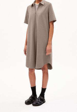 Robe kaki à manches courtes avec un col chemise et une fermeture éclair à mi-longueur. Associée à des sandales noires et des chaussettes. Coupe lisse et décontractée.