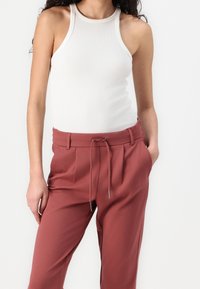 White ribbed halter top paired with high-waisted, rust-colored trousers featuring a drawstring waist and side pockets.