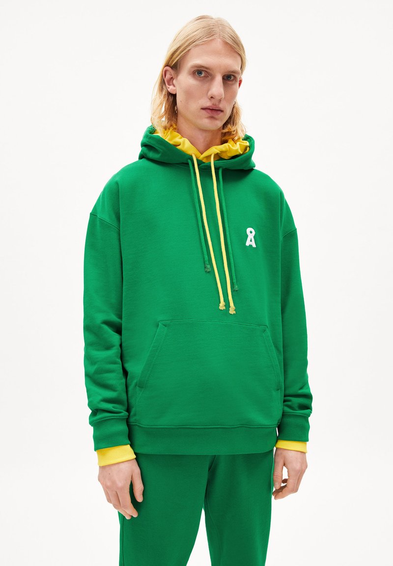 Grüne Kapuzenjacke mit gelben Akzenten und Kordeln, mit einem weißen Band-Logo auf der Brust und einer Fronttasche. Baumwollmaterial, lockere Passform.