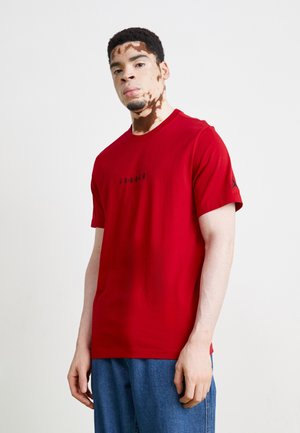 Rød bomulds T-shirt med rund hals og korte ærmer, der har et sort "JORDAN" grafik på fronten og et logo på en af ærmerne.