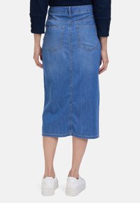 Jupe midi en denim bleu clair, taille cintrée avec deux poches arrière, détail cousu le long de l'ourlet, associée à des baskets blanches.