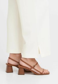 Sandales à talons carrés en bois marron avec des lanières. Les lanières sont fines et réglables, mettant en valeur une texture en cuir lisse.
